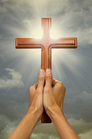Hands holding a wooden cross raised toward a bright light